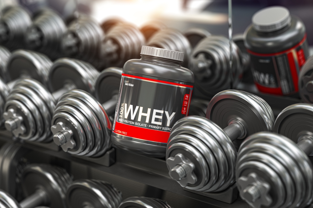 Whey protein powder in a row of dumbbells in a gym. Sports bodybuilding supplements and nutrition.